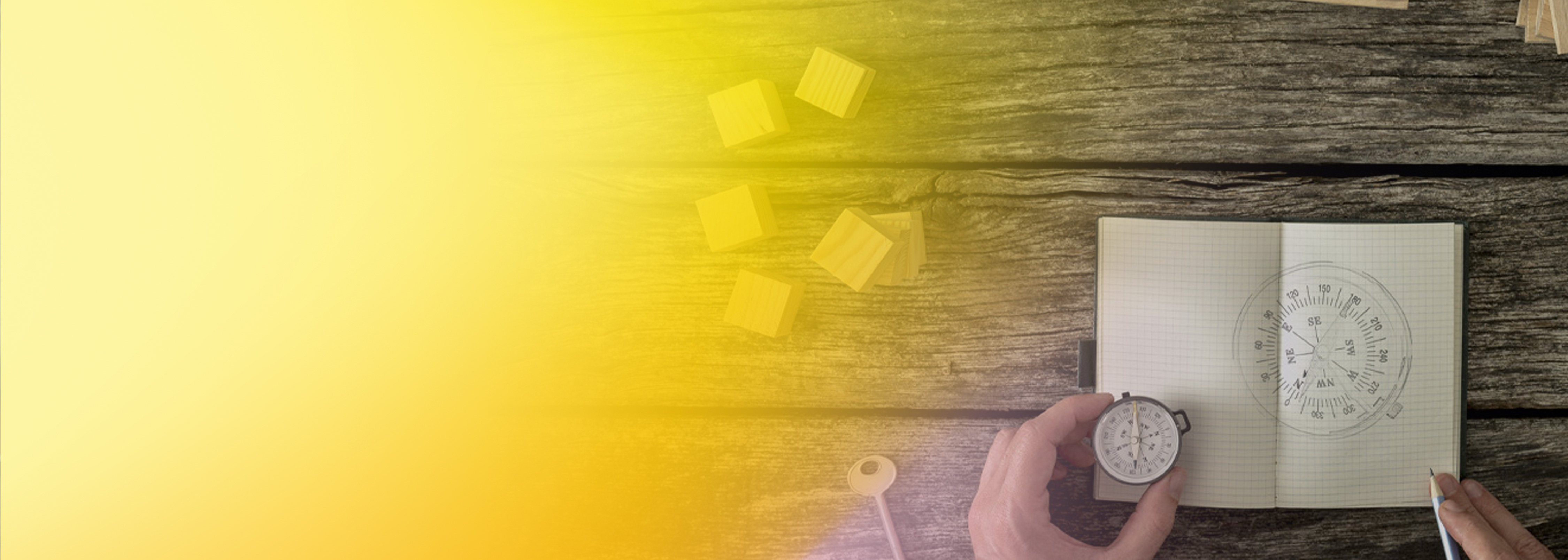 A top-down view of a hand holding a compass above an open notebook with a compass sketch, wooden blocks, and a pencil on a rustic wooden surface with a yellow gradient overlay. Symbolizes navigation and planning for AWS Lambda container development.