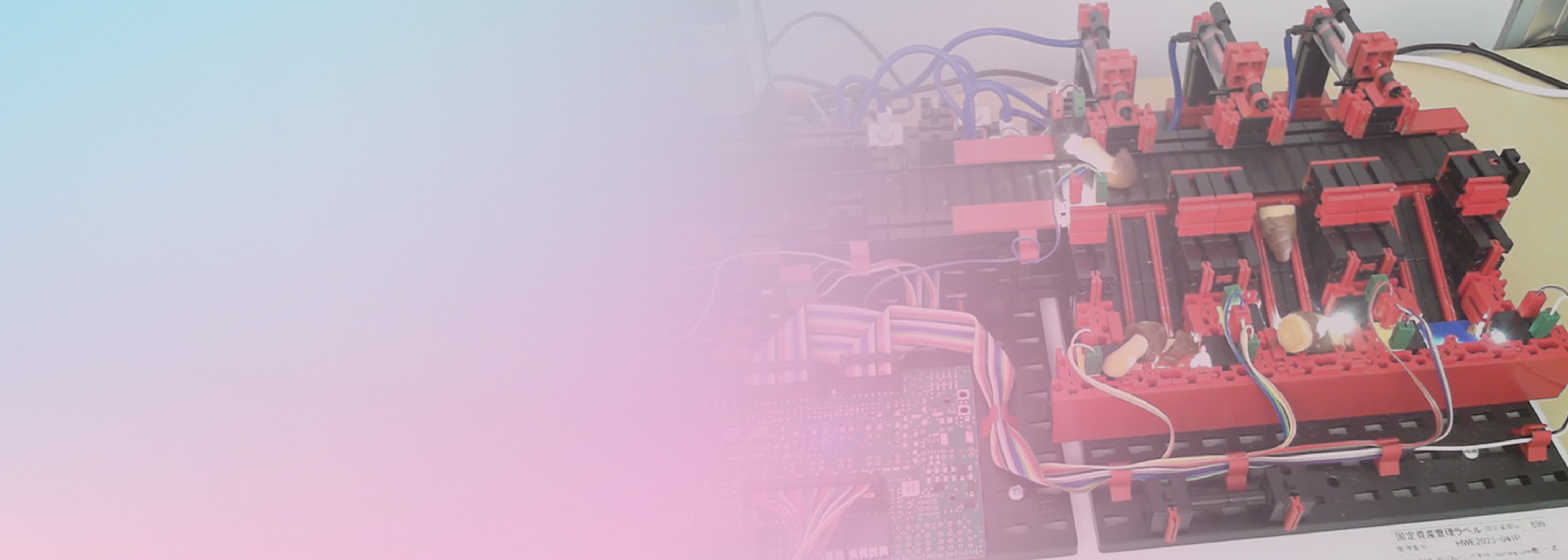 A robotics engineering project featuring a red and black mechanical system with connected electronic boards and wiring, set on a desk. The left side of the image is faded with a pastel gradient, emphasizing technical creativity and the mindset of innovation in engineering challenges.