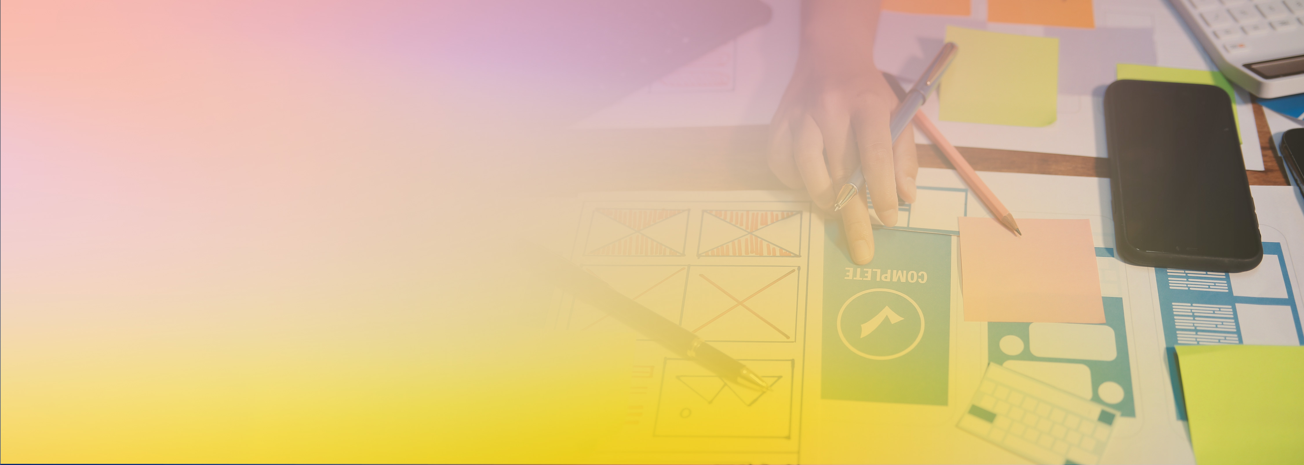 A partial view of a desk with development sketches, a smartphone, sticky notes, and a hand interacting with a 'COMPLETE' card, overlaid with a colorful gradient. Represents generative AI assisting in the development process.