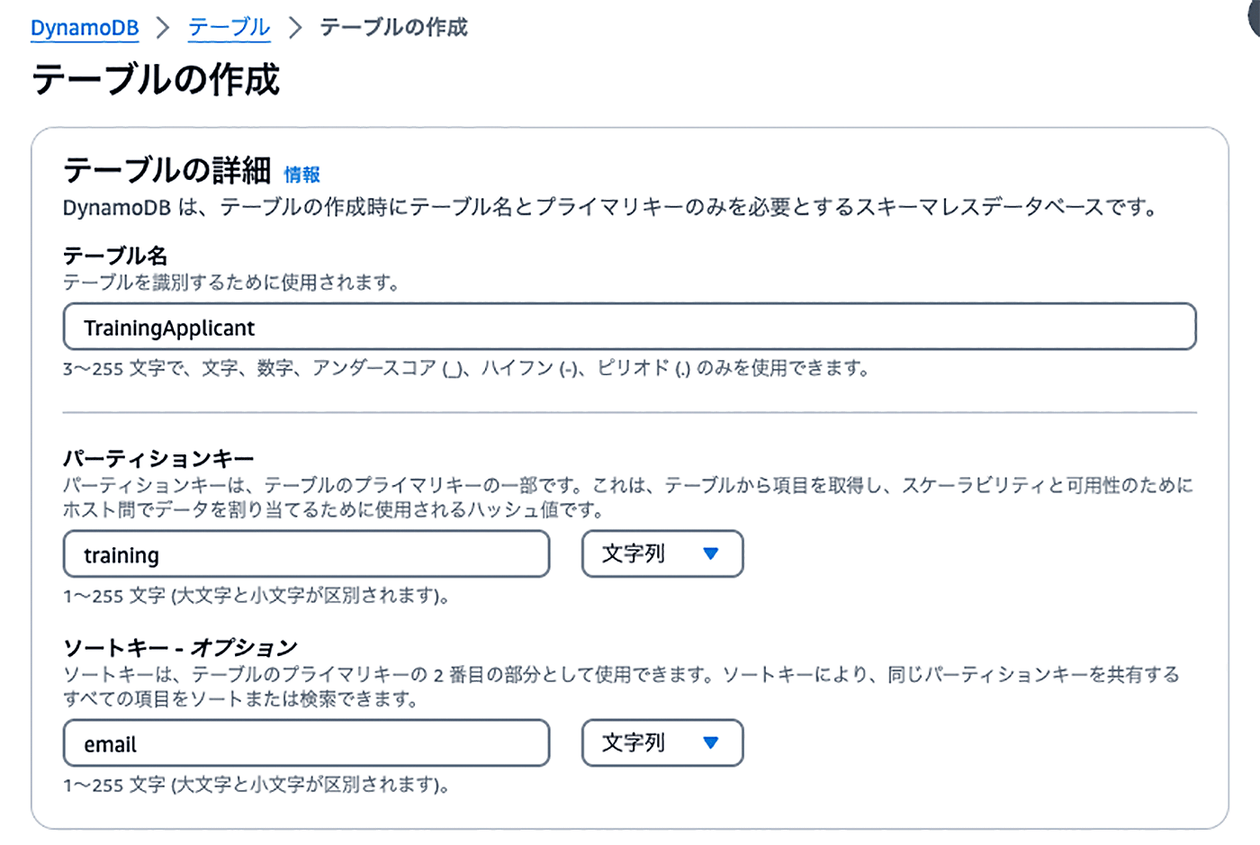 Screenshot of the Amazon DynamoDB table creation interface in Japanese, showing the setup for a TrainingApplicant table with 'training' as the partition key and 'email' as the sort key. The interface displays input fields for table configuration and instructions in Japanese.