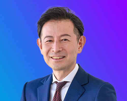A male speaker in a blue suit and tie, posing in front of a blue and purple gradient background at AWS Summit Japan.