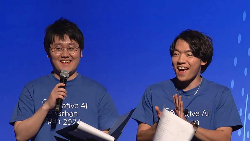 Two presenters wearing 'Generative AI Hackathon Japan 2024' shirts speak and clap on stage during an event, holding papers with a blue background.