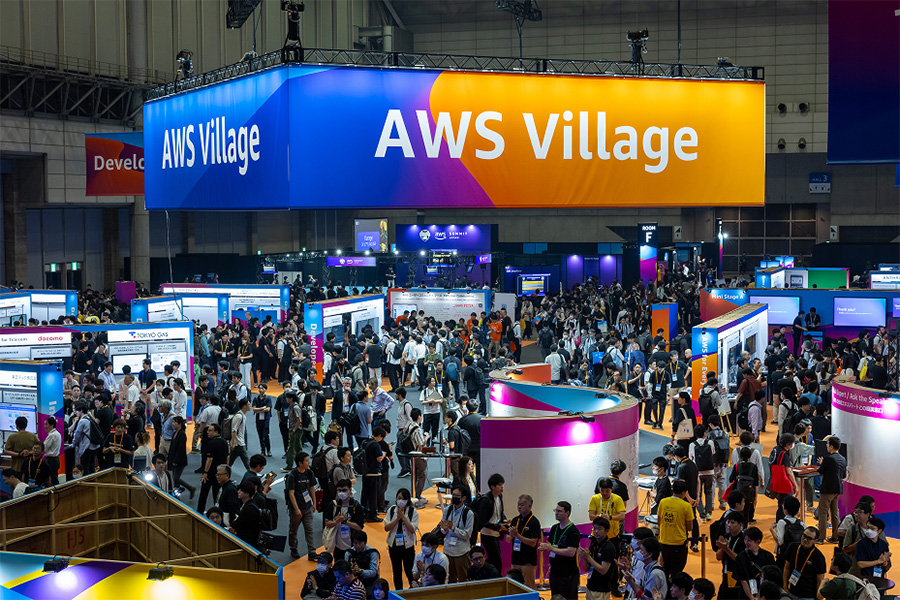 Large crowd attending AWS Village expo area at the Japan Summit 2025, with exhibition booths and event displays visible in a conference hall.