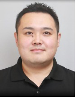 Portrait of a man in a black shirt with short black hair, facing the camera against a light background.