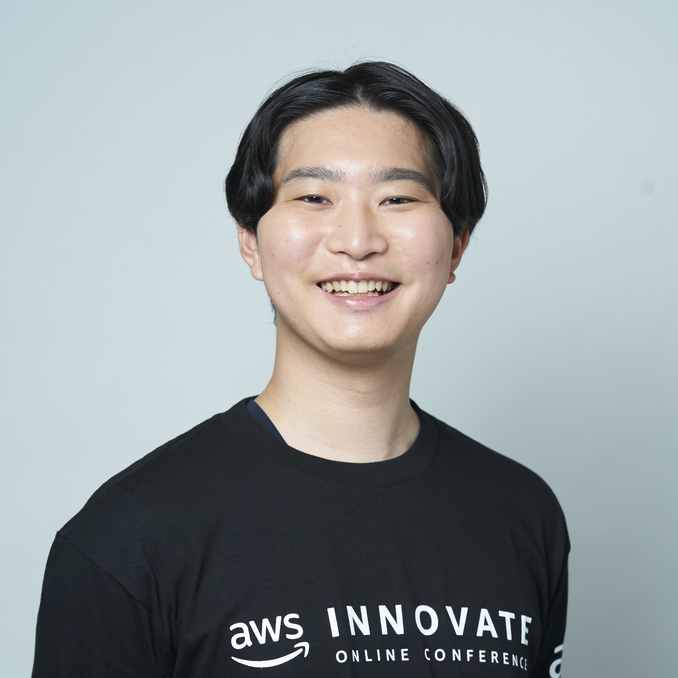 A participant in the AWS Innovate Online Conference, smiling and wearing an event t-shirt, portrait against a plain background.