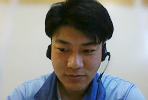 A man wearing a blue shirt and a headset, appearing to be in a virtual meeting or customer support setting.