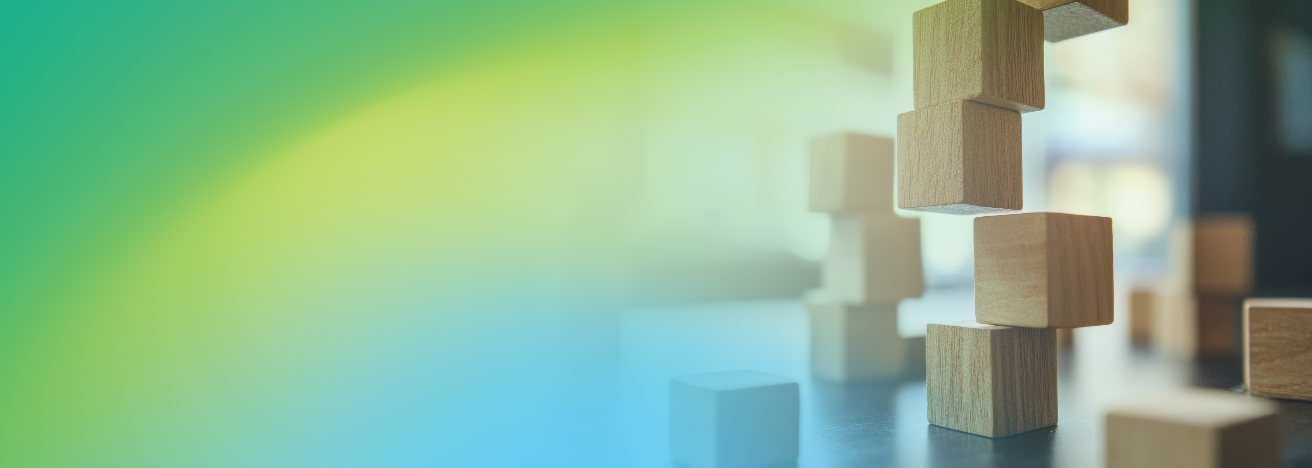 Several wooden blocks are stacked and scattered on a surface, with a soft green, yellow, and blue gradient background. The image evokes creativity, collaboration, and construction, making it suitable for events or teamwork-related themes.