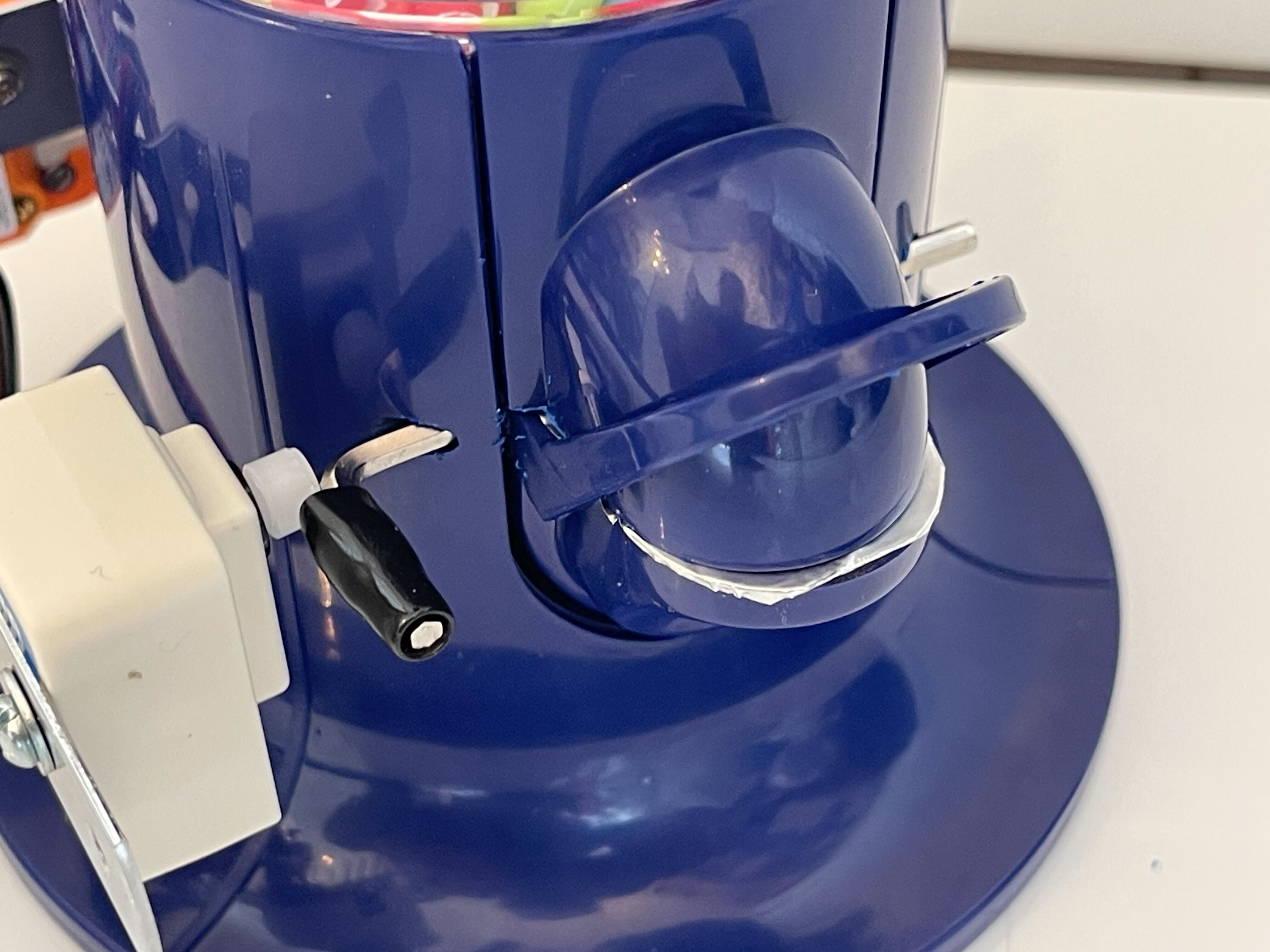 A close-up image of a blue mechanical or electrical device with a lever and white component, likely part of a machine or appliance, placed on a white surface.