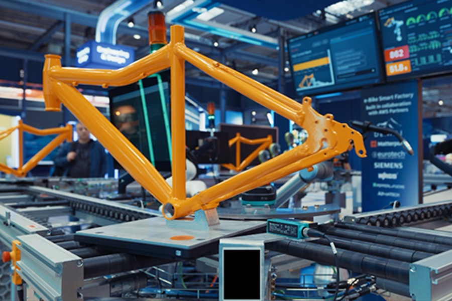 Yellow bicycle frame on an automated assembly line in a high-tech factory setting with digital screens in the background.