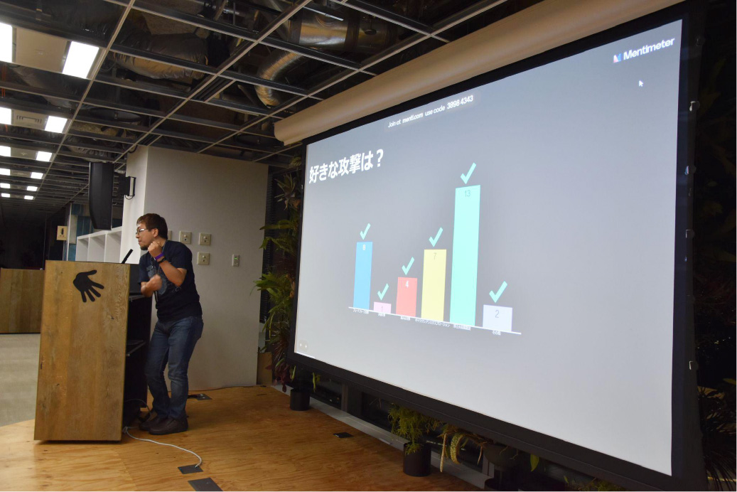 A speaker presents at JAWS DAYS 2023 event with a security-related Mentimeter poll displayed on a large screen. The slide shows a bar chart with responses, and the presentation is conducted in a modern conference room.