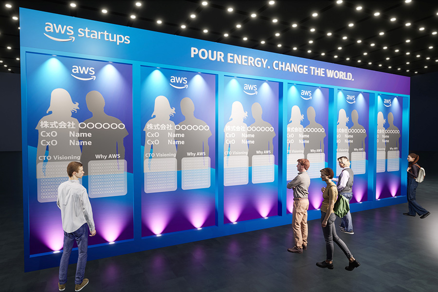 A photo of the AWS startups booth at AWS Summit 2025, featuring a large blue and purple exhibition wall with 'AWS startups' branding and the phrase 'POUR ENERGY. CHANGE THE WORLD.' Several people are standing and viewing information panels, which highlight startup details and showcase areas for company names, CTO visioning, and reasons for choosing AWS.