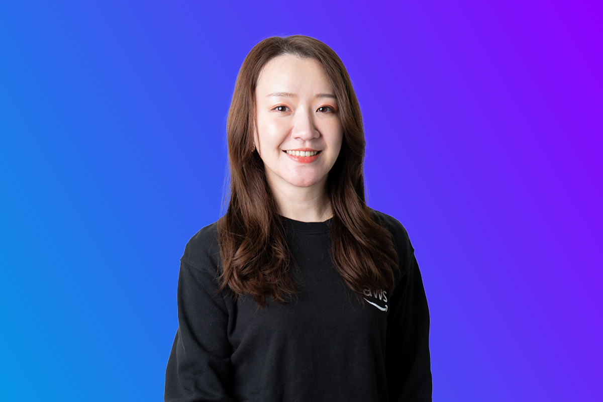 A portrait of an AWS team member in a black shirt with 'AWS' branding, in front of a blue and purple gradient background, associated with the AWS Japan Summit 2025.