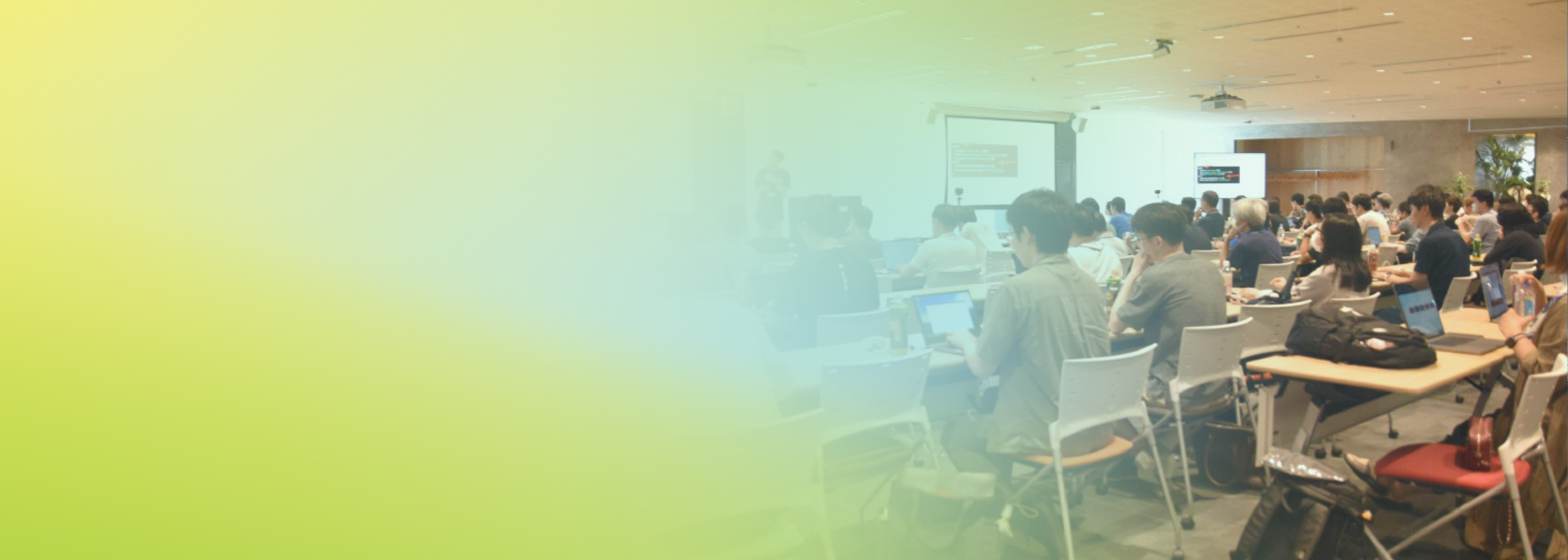 A wide view of a seminar room filled with attendees at computers, listening to a speaker during a Security JAWS Days event, with a soft yellow-green gradient overlay on the left.
