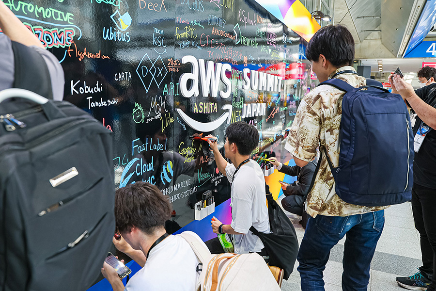 Attendees write messages and signatures on a colorful wall display at the AWS Summit Japan 2025 event venue.