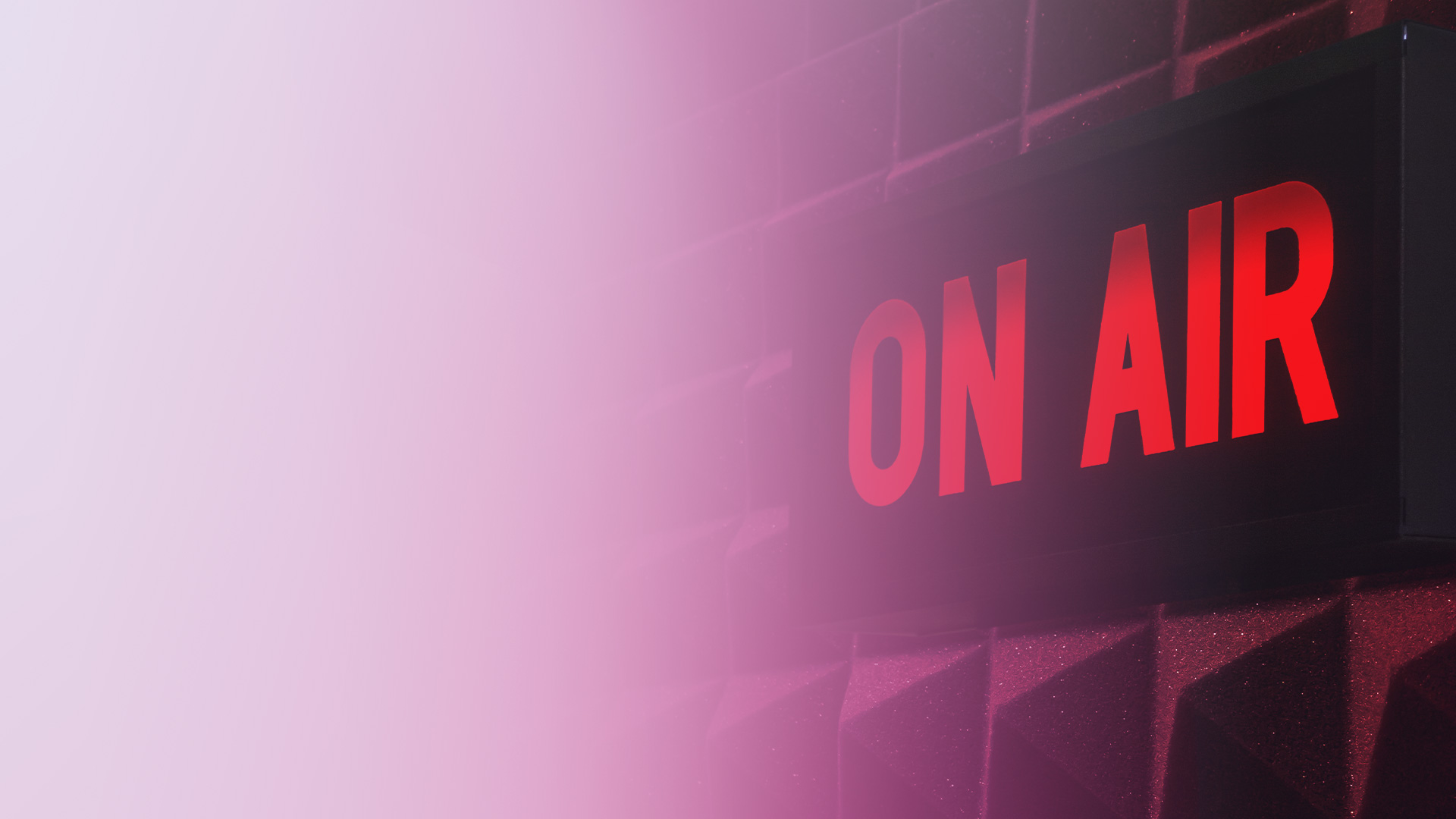 A studio 'On Air' illuminated sign with red letters on a soundproof wall, bathed in pink lighting, representing a live broadcast or live show environment.