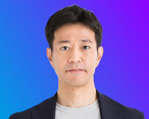 Portrait photograph of a man in a navy blazer and light sweater, shown against a blue and purple gradient background, taken for AWS Summit Japan event.