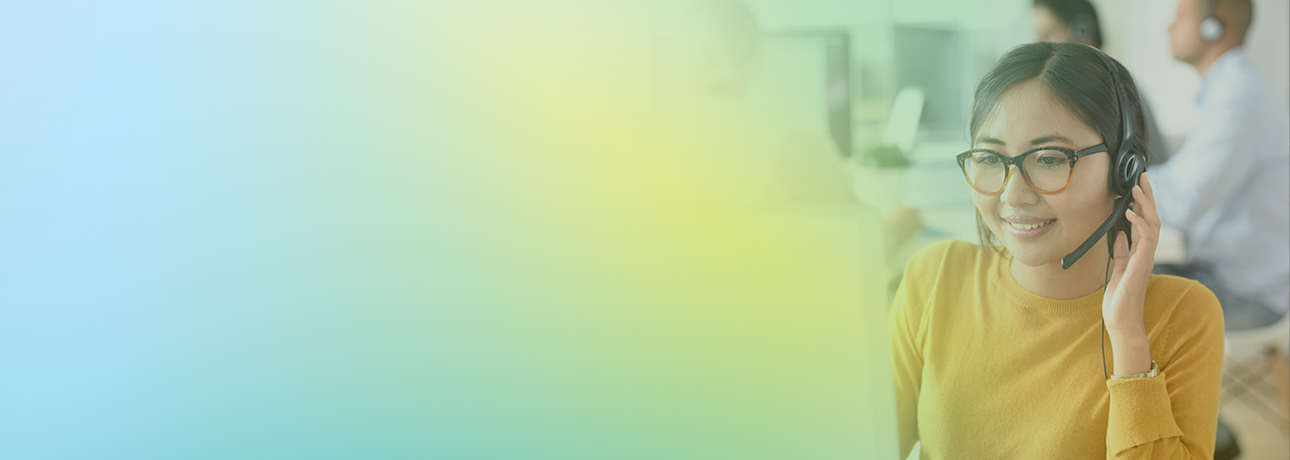 A woman wearing a headset and glasses is smiling and working at a help desk, representing customer support using Amazon Connect in a modern contact center environment.