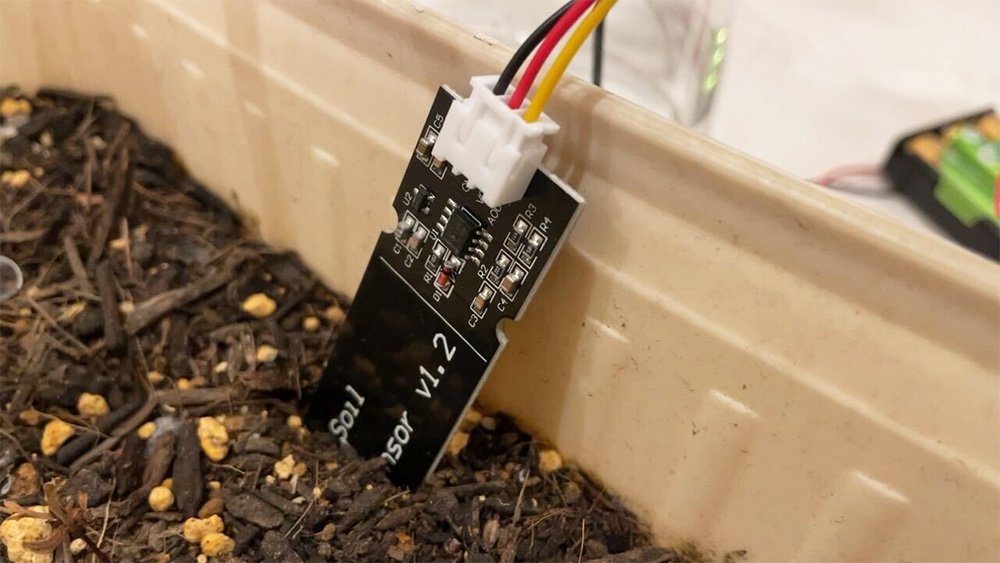 A close-up photo of a soil moisture sensor inserted into soil in a planter, illustrating smart gardening and IoT-based environmental monitoring.
