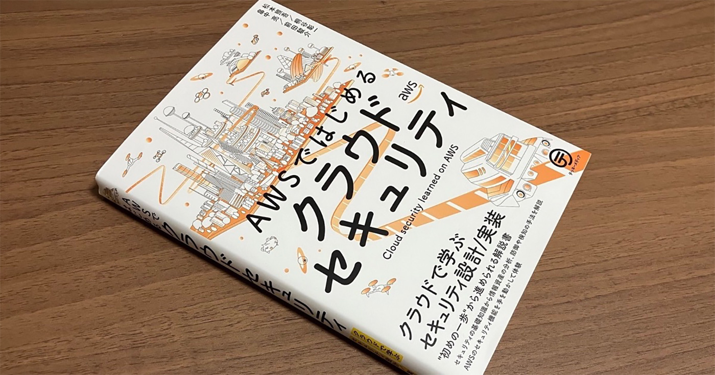 Cover of the Japanese book 'AWSではじめるクラウドセキュリティ' (Cloud Security Learned on AWS), featuring illustrations of technology and cloud concepts on a wooden surface.