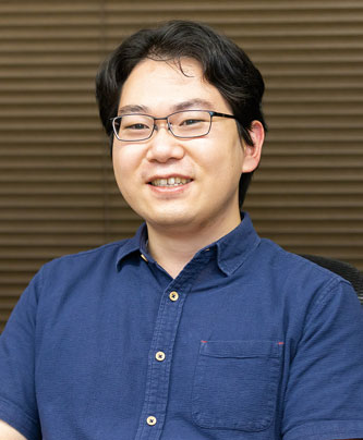 A man wearing glasses and a blue shirt, smiling, seated in front of a brown background. This image is used for a case study speaker profile.