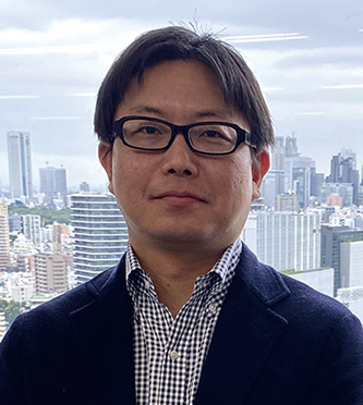 A businessman wearing glasses and a suit stands in front of a modern cityscape background with tall buildings and a cloudy sky.