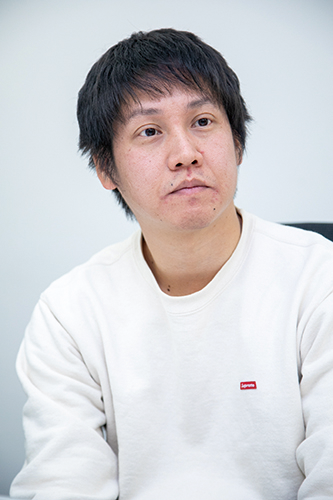Portrait of an individual from ZOZO Technologies, featured in an interview. The person is wearing a white sweater and appears in a professional interview setting.