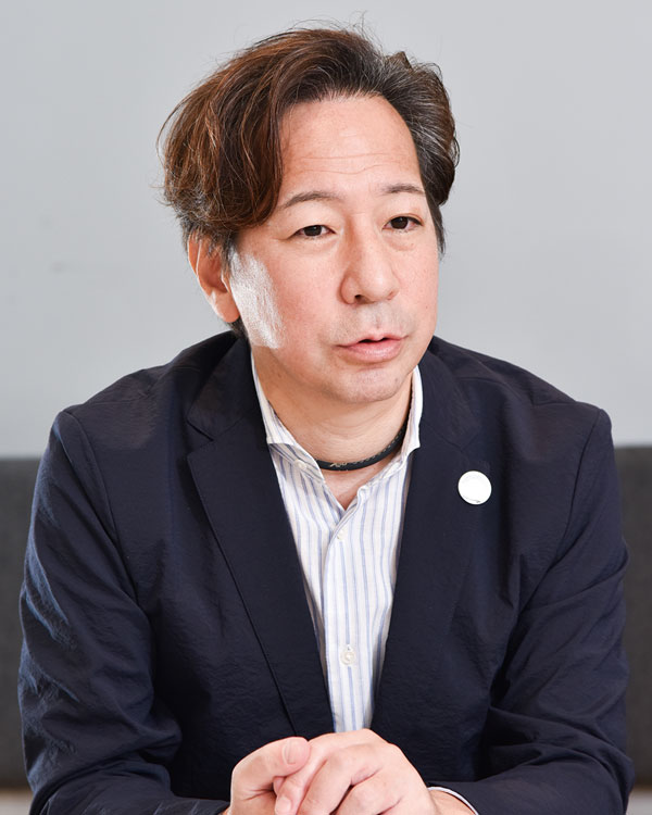 Portrait photo of a Mitsubishi Soko case study speaker in a business setting, wearing a blazer and striped shirt, seated and speaking.