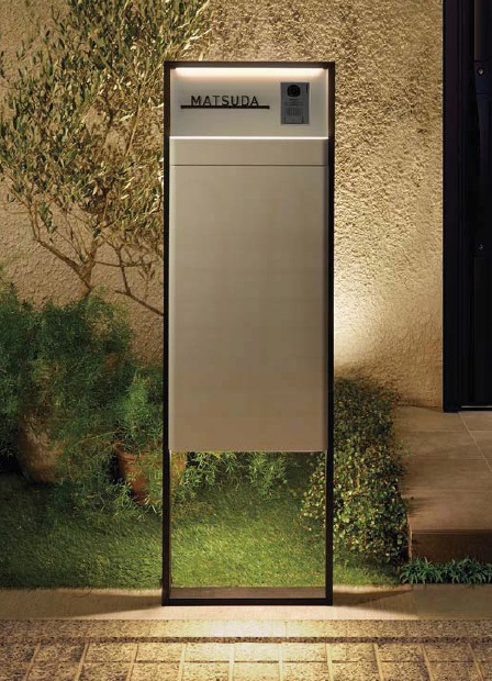 A modern, illuminated mailbox labeled "Matsuda," set against a textured wall with greenery in the background.