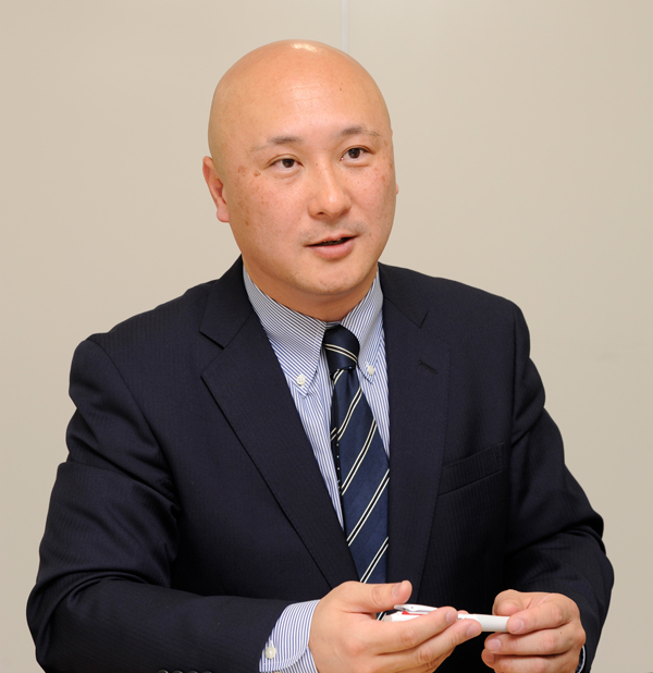 A businessman in a suit holding a pen during an interview or business meeting setting.