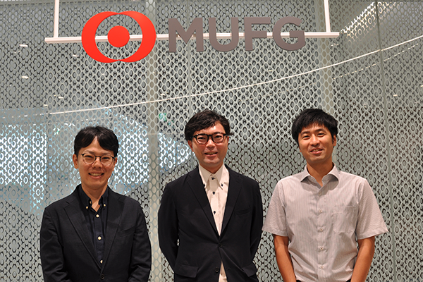 Three MUFG team members posing and smiling in front of a MUFG sign and decorative background.
