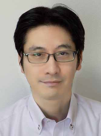 Portrait photo of a man with glasses and dark hair, wearing a light-colored collared shirt, in front of a plain background.