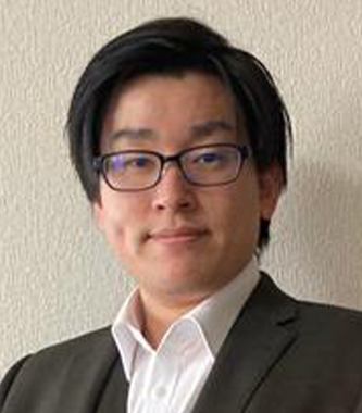 Portrait of a business professional in a suit, wearing glasses, with short dark hair, standing against a light textured wall. (Konica Minolta case study image)