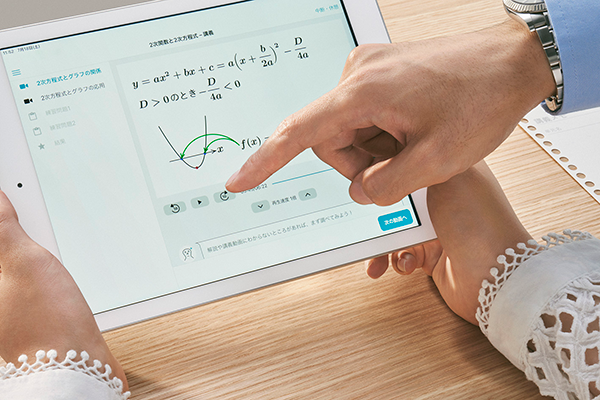 A close-up of two people using a tablet for a math lesson, featuring a quadratic equation and graph in Japanese. The image illustrates the use of digital learning tools in education, as part of an Atama Plus case study.