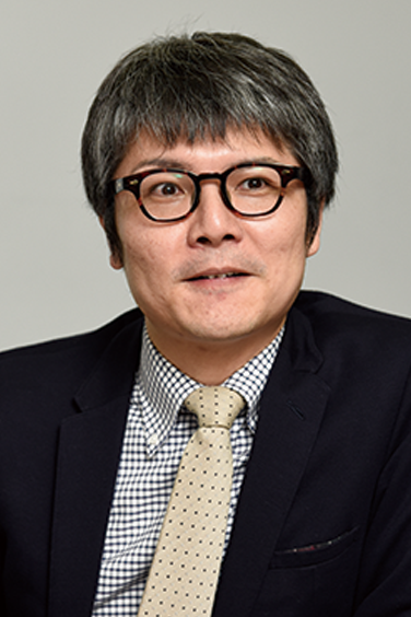 Portrait of a businessman wearing glasses, a suit, and a tie, looking forward against a neutral background.