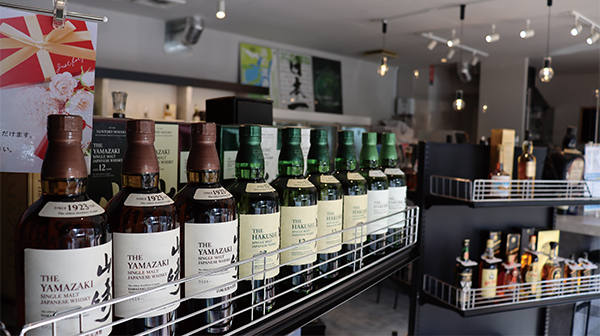 A row of Japanese whisky bottles, including The Yamazaki and The Hakushu, displayed on a shelf inside FiveNeeds Liquor Store. The setting is modern with additional bottles and spirits visible in the background. Case study showcasing AWS solutions for retail management.