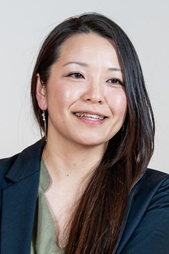 A person with long dark hair wearing a black blazer and green top.