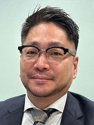 A person wearing a suit and tie against a light green background.