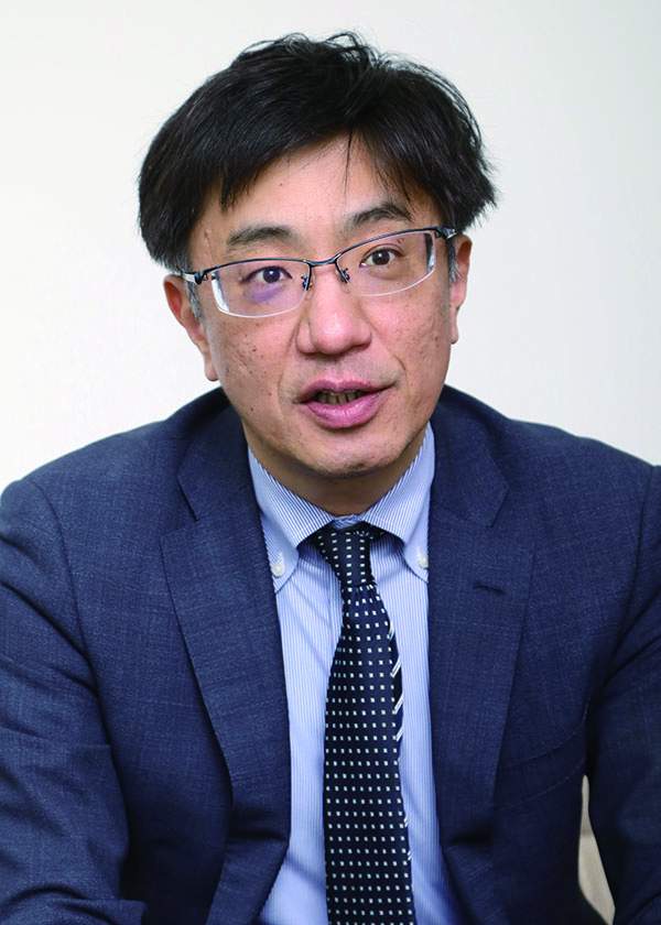 A portrait photograph of a man wearing glasses and a business suit, facing forward against a plain background.