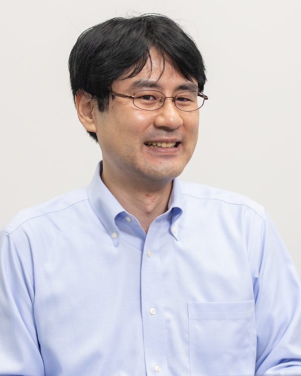Portrait of a man wearing glasses and a light blue shirt, smiling in front of a plain background.