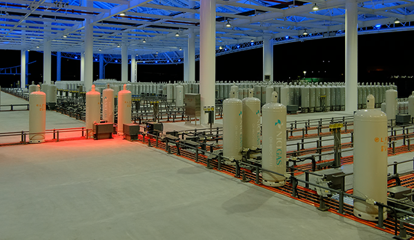 Large, modern industrial site with multiple gas storage tanks at night, brightly lit under a covered structure. This image is used for an AWS case study featuring NICIGAS.