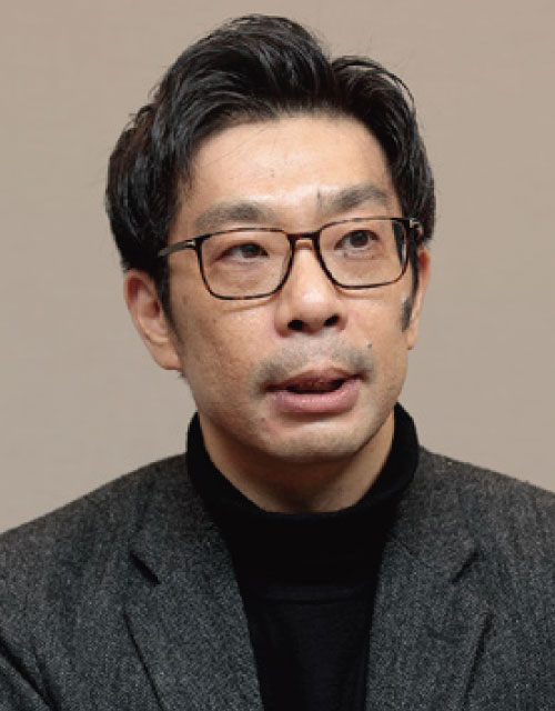 A person wearing a dark turtleneck and gray blazer against a neutral background.