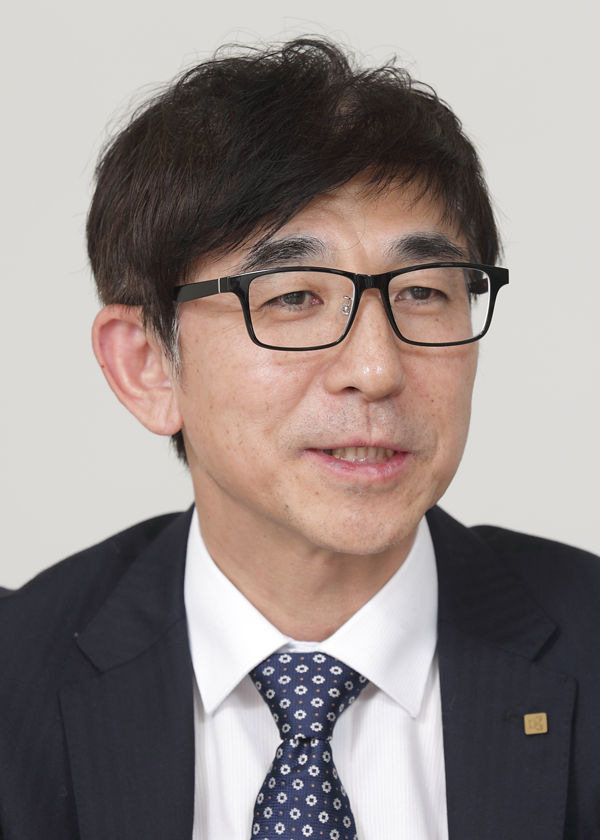 A portrait of a businessman wearing glasses and a suit, looking slightly off-camera, with a neutral background.