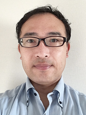 A portrait photo of a person wearing glasses and a light blue shirt, facing forward against a plain light background.