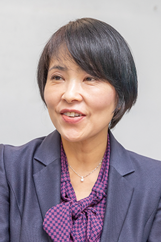 A portrait of a business professional woman with short black hair, wearing a dark blazer and patterned blouse, against a light background.