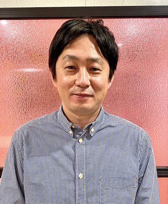 Portrait photo of a speaker in a checkered shirt, standing in front of a textured pink background, used for RareJobTech solution case studies.