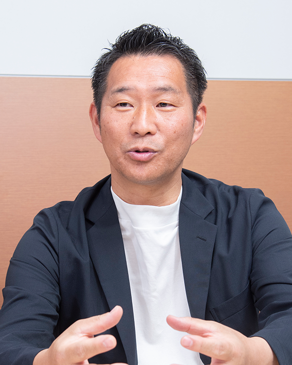 A professional portrait of a person in a business setting, featured in a KDDI case study interview.