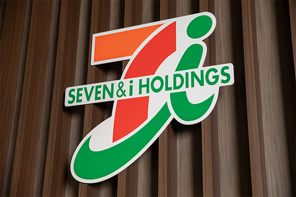 The Seven & i Holdings logo mounted on a wooden wall background.