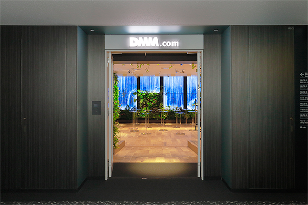 Entrance to the DMM.com office featuring modern design and vibrant greenery, with digital screens and lush plants creating a welcoming atmosphere.