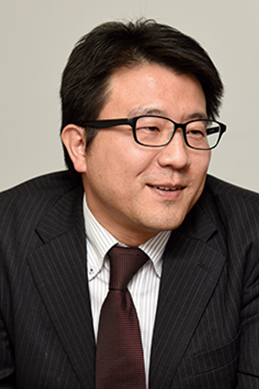 Business portrait of a man wearing a suit, tie, and glasses, facing left and smiling.