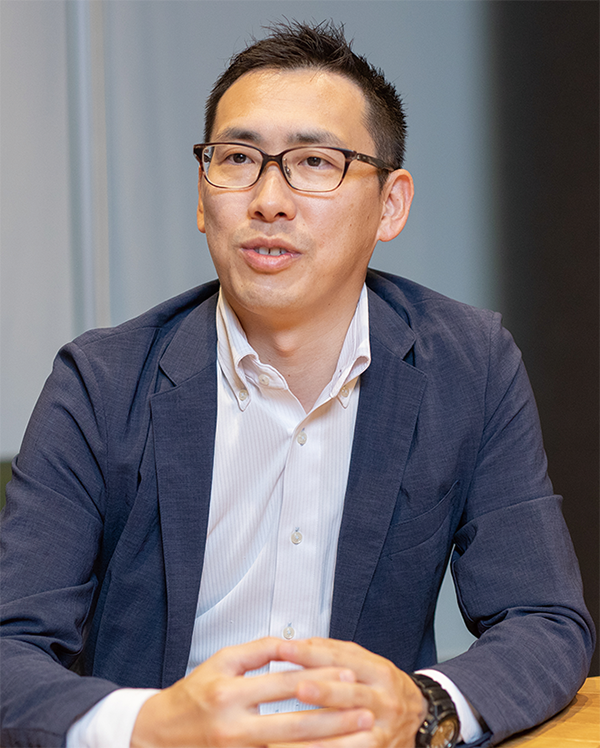 A business professional in a suit with glasses sits at a table, engaging in an interview and discussion.